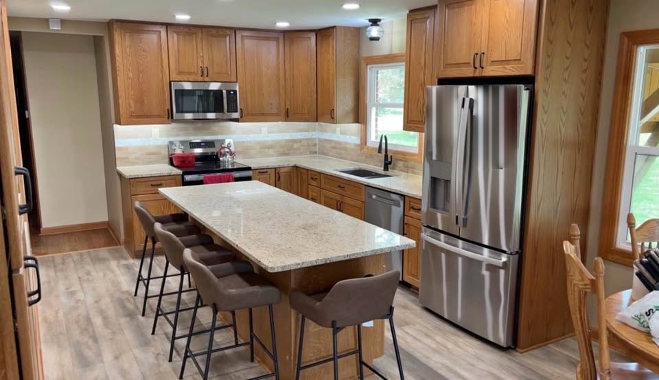 A natural oak kitchen with a long island, four barstools, and a stainless range
