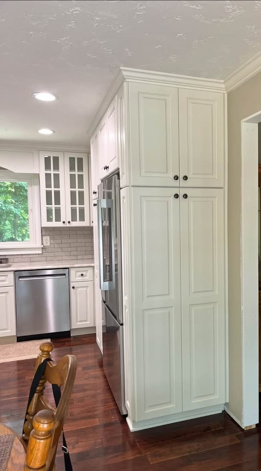 A tall white pantry cabinet with raised-panel doors and black knobs beside a built-in refrigerator