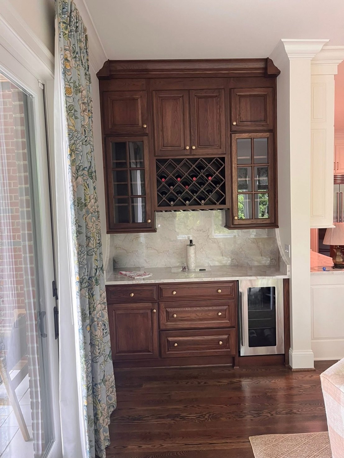 A dark-stained wet bar with glass-front cabinets, a built-in wine rack and a stainless beverage fridge, beside a garden door