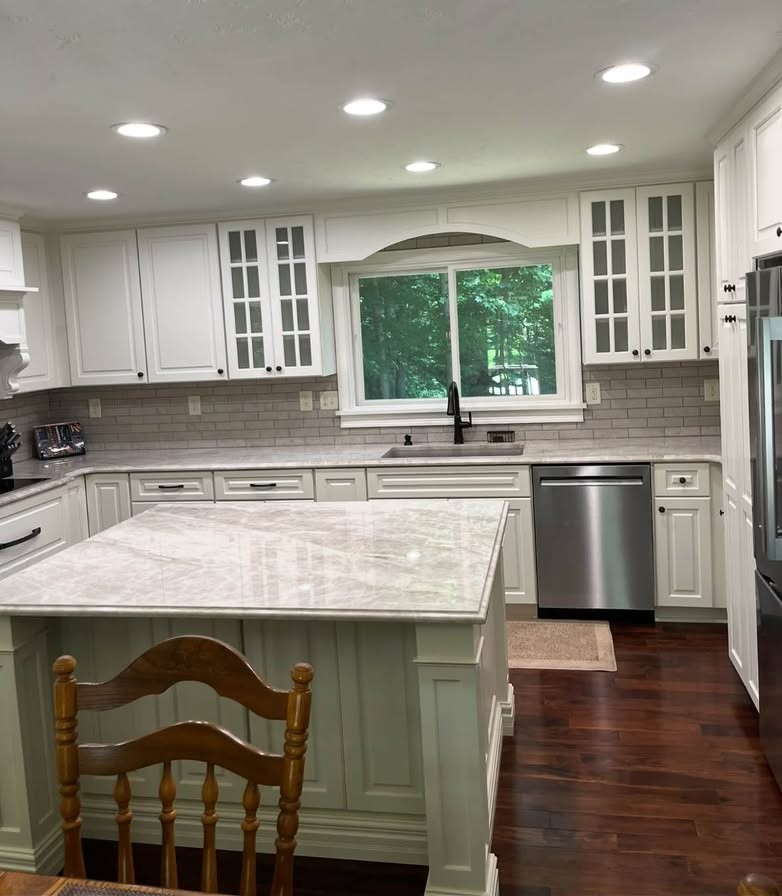 A white raised-panel kitchen with glass-front upper cabinets and a painted sage island