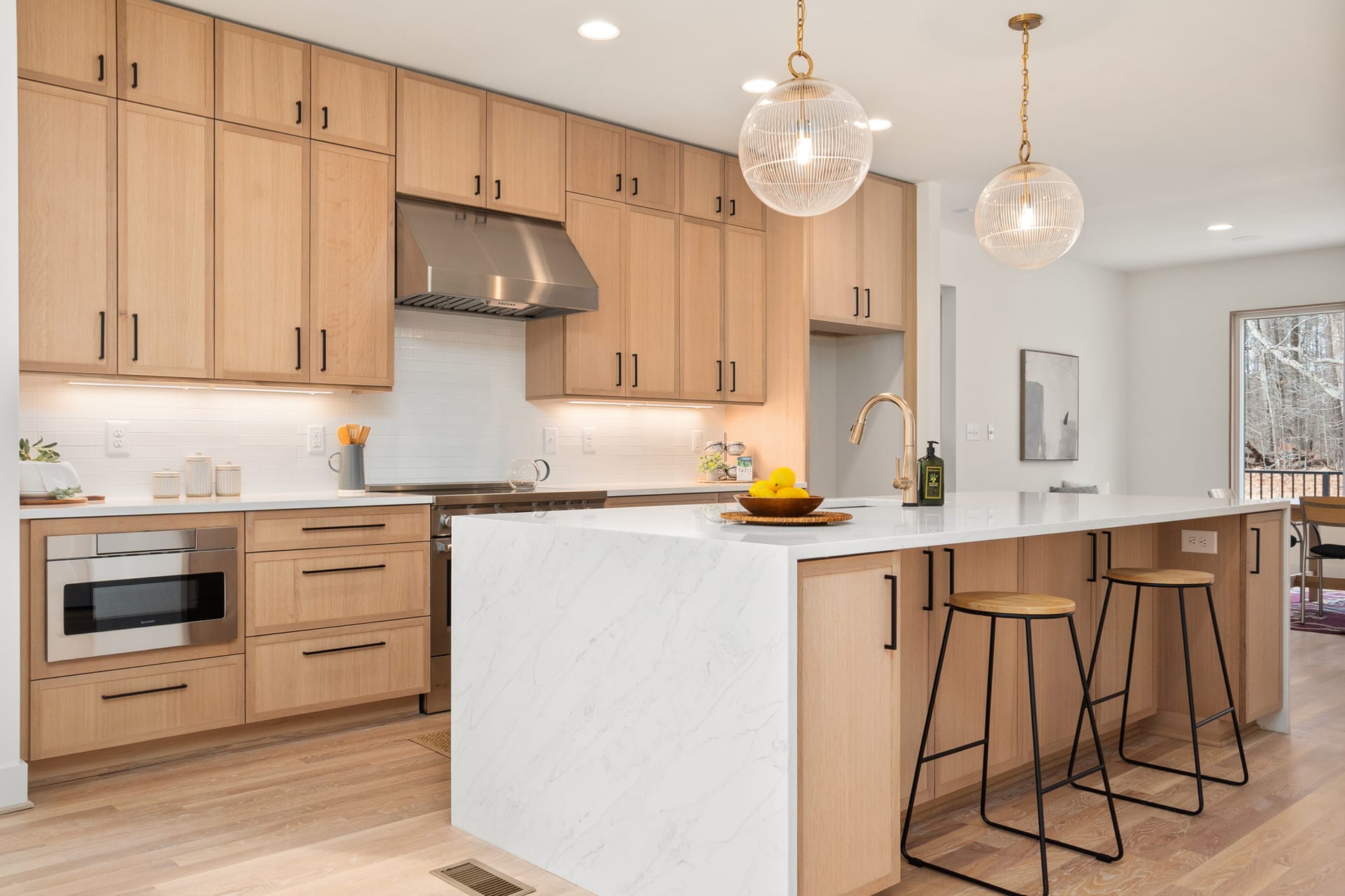 A pale oak kitchen with flat-panel doors, black pulls, and a long island with two stools