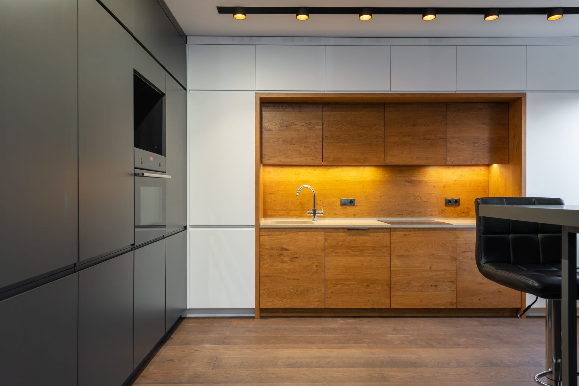 A kitchen with wood-grain cabinets set into a wall of white and charcoal flat-panel cabinets
