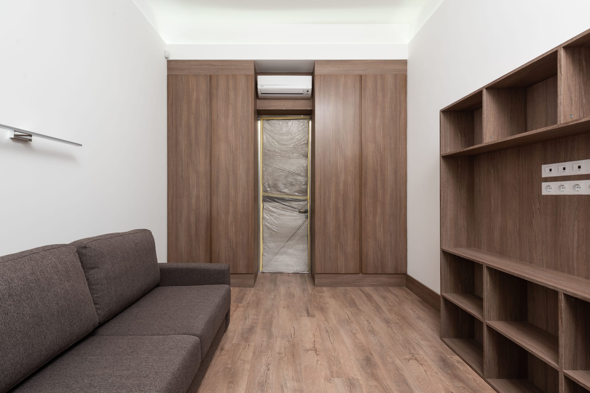 A room with a wall of tall wood-grain closet doors and open wood shelving